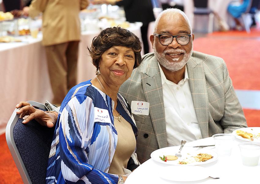 Two people sitting at table at event smiling.