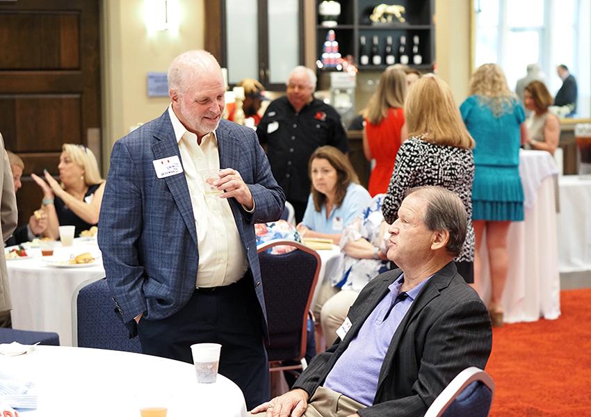 Man standing and speaking to another man sitting at a table.