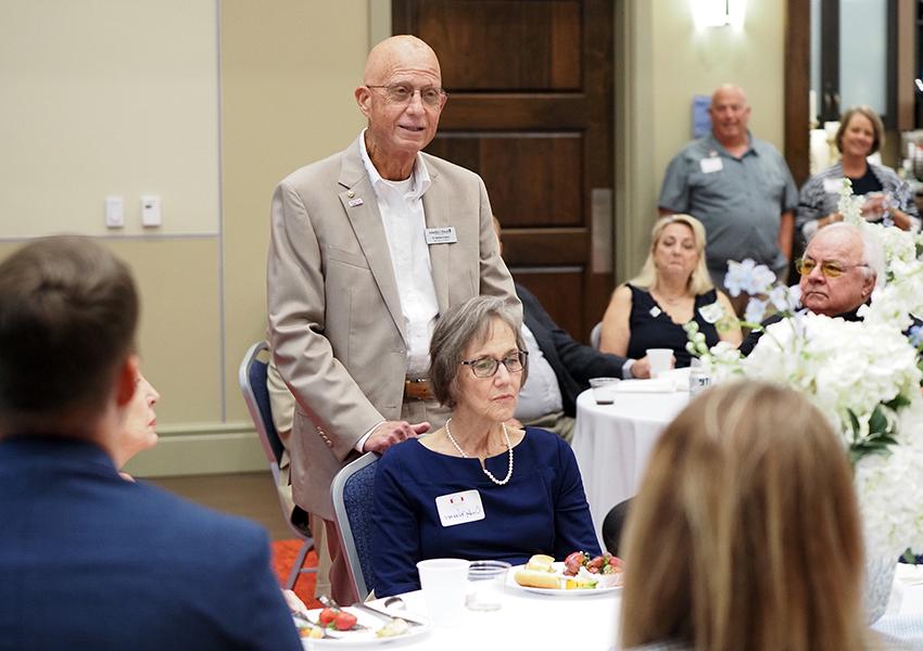 Man standing behind chair speaking at event.