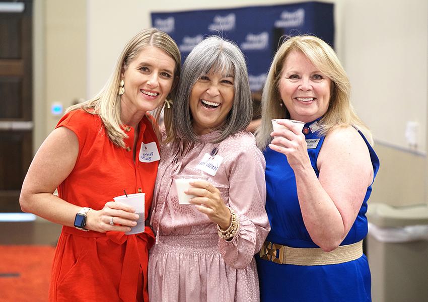 Karen Edwards with two alumni smiling all wearing dresses.