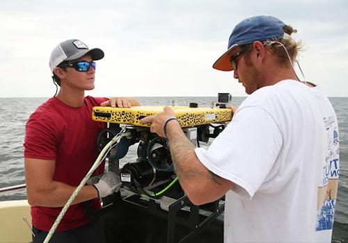 Two students working on boat doing research.