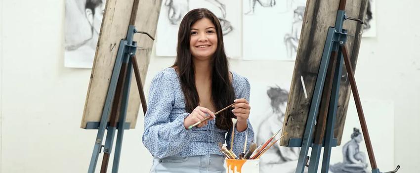 荣誉 student in paint studio holding a paint brush.